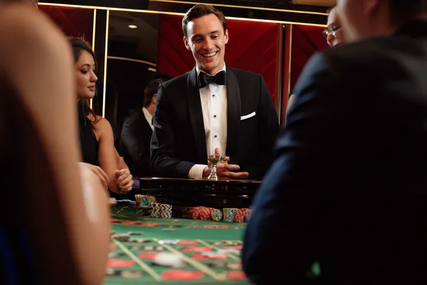 SPINARAA Live Casino — Join thrilling real-dealer tables A professional dealer in a tuxedo greeting players at the roulette table, symbolizing the authentic live casino feel at SPINARAA.