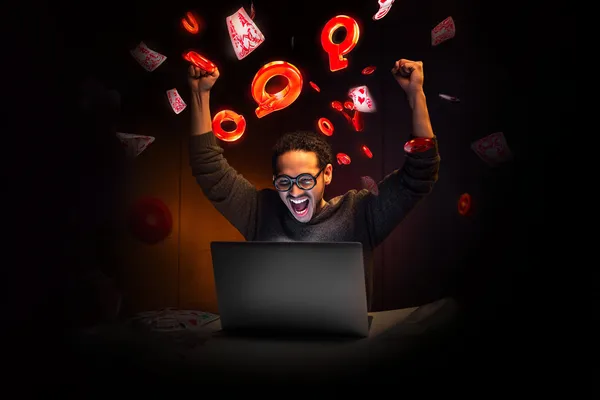 A man celebrating a winning moment on his laptop while gaming symbols float around him, capturing the excitement of SPINARAA games.